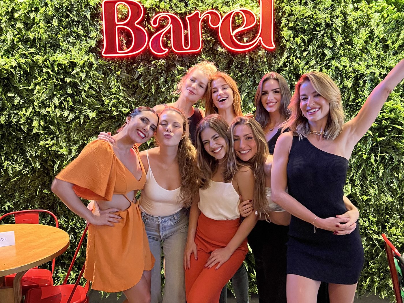 Grupo de amigas festejando un cumpleaños en el Barel frente a la pared de plantas y al cartel de neón