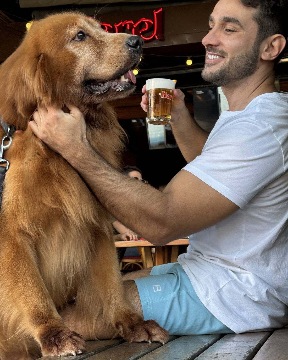 Cliente tomando un chopp en la vereda del Barel con el perro en brazos, bajo el cartel rojo