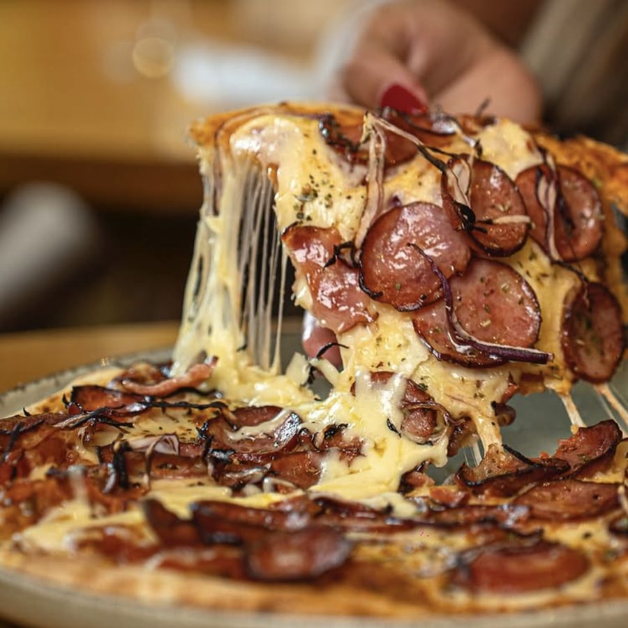 Fatia de pizza de calabresa artesanal do Barel sendo puxada do prato, com o queijo derretendo